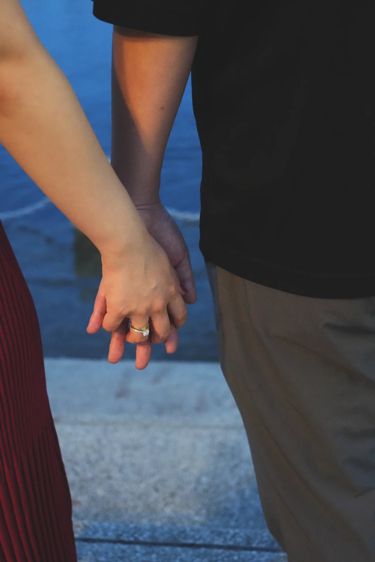 海の前で手を繋ぐカップルと結婚指輪の輝き